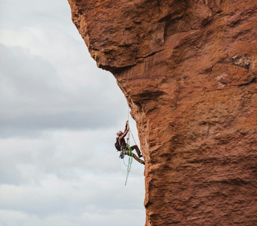 man in black shorts climbing brown rock formation during daytime